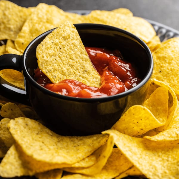 A black bowl of red salsa with a tortilla chip dipped in it, surrounded by more chips.
