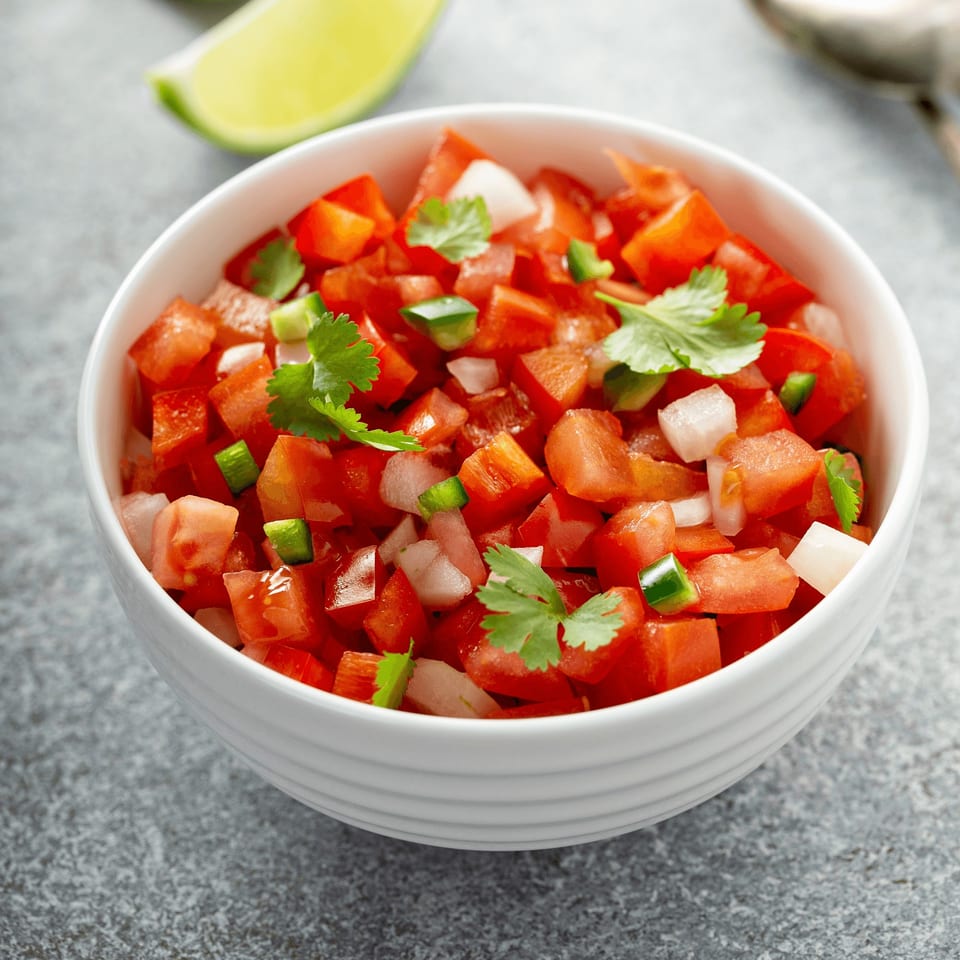 Freshly made pico de gallo with diced tomatoes, onions, cilantro, and jalapeños in a white bowl.