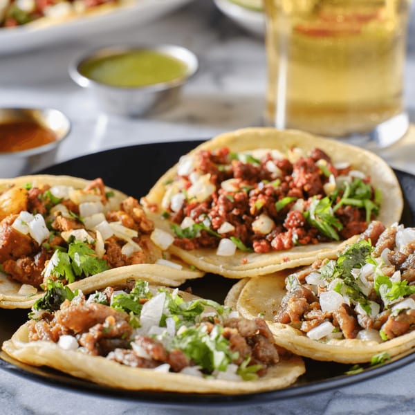 A black plate filled with various Olivo Taco street tacos, garnished with cilantro and onions.