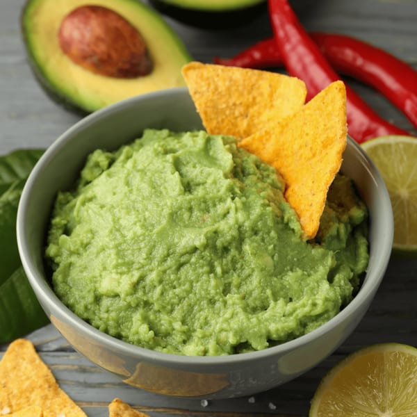 Fresh guacamole with tortilla chips, avocado, red chilies, and lime on a wooden table.